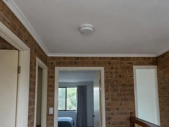 White smoke alarm on a ceiling in a brick-walled home interior in Maudsland
